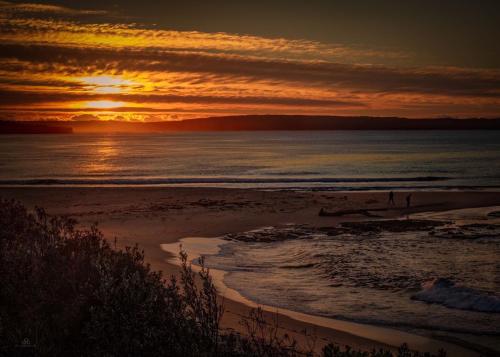 a sunset view of a beach with a body of water at Jervis Bay Holiday Cabins in Sussex Inlet