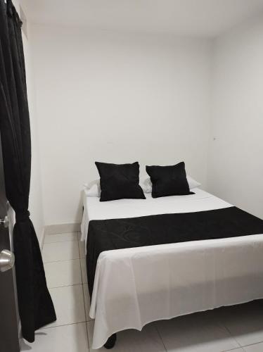 a white bed with two black pillows on it at HOTEL BLACK & WHITE in Cali