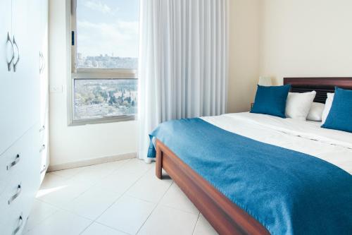 a bedroom with a bed with blue sheets and a window at Almog Haifa Israel Apartments מגדלי חוף הכרמל in Haifa