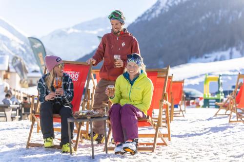 a man and two women sitting in chairs in the snow at Hotel Alegra in Livigno