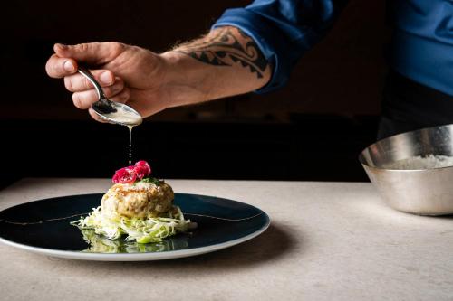 a hand holding a spoon over a plate of food at Falkensteiner Family Resort Lido Superior in Chienes