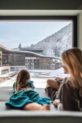 two girls sitting on a bench looking out a window at Falkensteiner Family Resort Lido Superior in Chienes