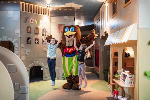 two children standing next to a mascot in a room at Falkensteiner Family Resort Lido Superior in Chienes
