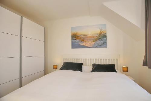 a bedroom with a white bed and a painting on the wall at Haffblick Wohnung 48 in Boltenhagen