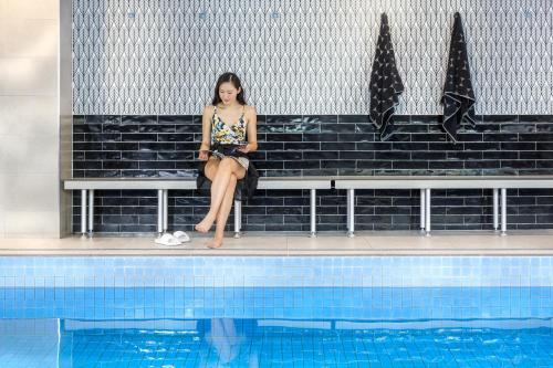 a woman sitting on a bench next to a swimming pool at Meriton Suites Chatswood in Sydney