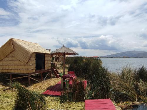 a hut with a table and an umbrella next to a body of water at Quechua lodge Titicaca in Puno