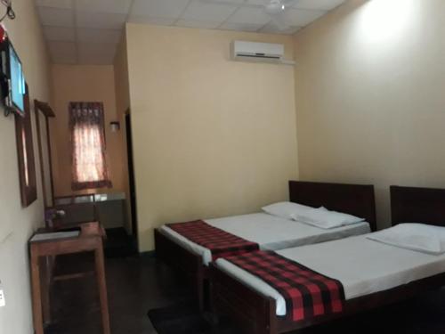 a room with two beds and a table in it at Katagamuwa Rest in Kataragama