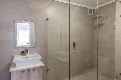 a bathroom with a shower with a sink and a mirror at Waters Edge Apartments in Cape Town