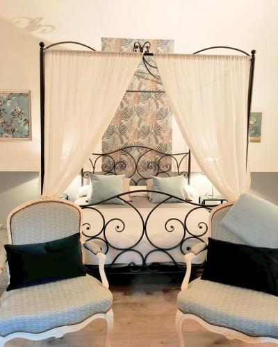 a bedroom with a bed with curtains and two chairs at Le Mas d'Hermès in Plan-dʼOrgon