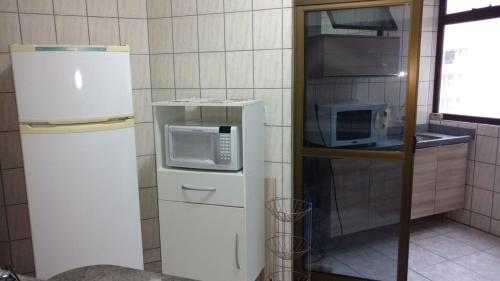 une petite cuisine avec un réfrigérateur et un micro-ondes dans l'établissement Apartamento Meia Praia Itapema, à Itapema