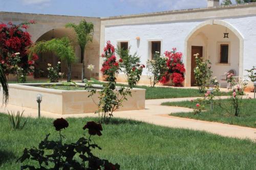 a building with a garden with red flowers and a fountain at Masseria Zambardo in San Vito dei Normanni