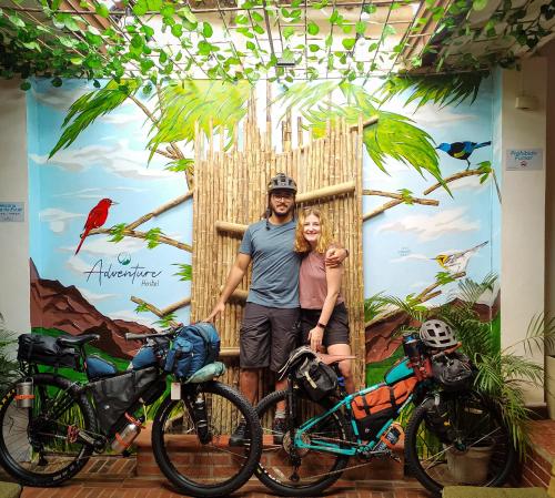 Ein Mann und eine Frau stehen vor einer Wand mit zwei Fahrrädern in der Unterkunft ADVENTURE Hostel in San Gil