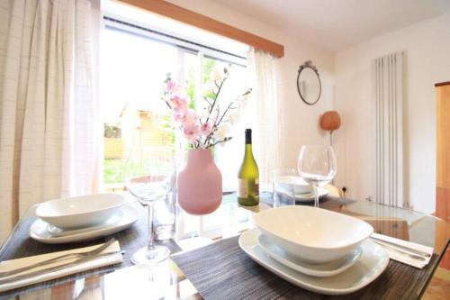 stół jadalny z talerzami i kieliszkami oraz wazon w obiekcie Cheerful Two-Bedroom Residential Home w Oksfordzie