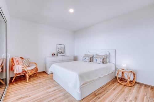 a white bedroom with a bed and a chair at Casa das Voltinhas in Ponta do Sol