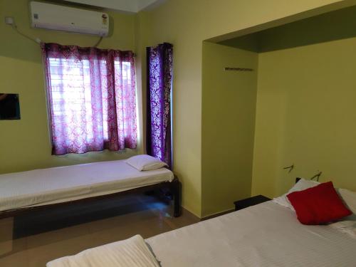 a bedroom with two beds and a window with purple curtains at Radha Rani lodge in Siliguri