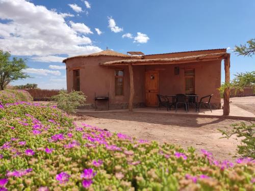 una pequeña casa con flores púrpuras delante de ella en Cabañas Larache, en San Pedro de Atacama