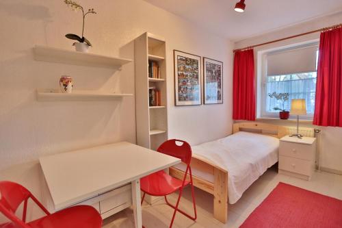 een kleine slaapkamer met een bed, een bureau en rode stoelen bij Haus Parkblick Parkblick Appartement 1 in Scharbeutz