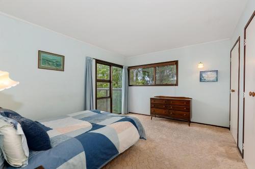 Te Whare Rākau - Paihia Holiday Home في بيهْيا: غرفة نوم بسرير وخزانة ونوافذ