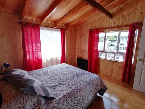 アンクードにあるDepartamentos y Cabañas Ancudのベッドルーム1室(ベッド1台付)、赤いカーテン付きの窓2つが備わります。