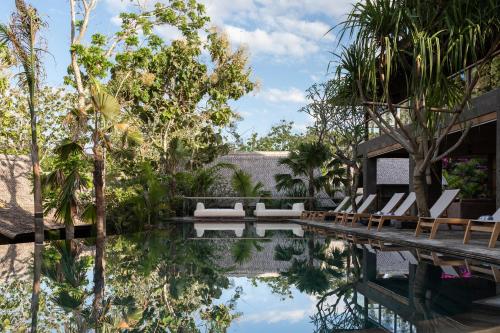 a resort pool with lounge chairs and trees at The Asa Maia - Bespoke Wellness Resort in Uluwatu
