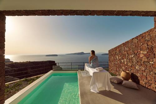 a woman sitting on a balcony looking out at the ocean at Coco-Mat Hotel Santorini in Akrotiri