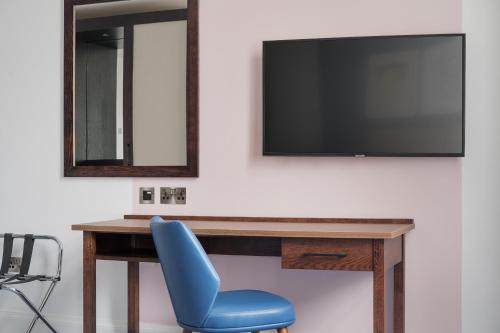 a desk with a blue chair and a television on a wall at voco Grand Central Glasgow by IHG in Glasgow