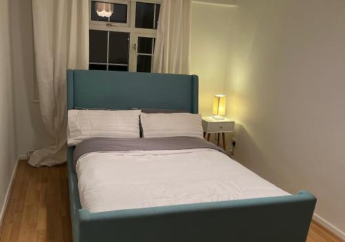 uma cama azul num quarto com uma janela em Lovely 2 bedroom apartment with parking space em Londres