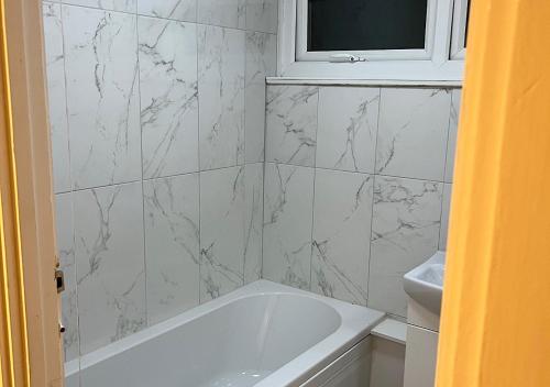 uma casa de banho com uma banheira branca e uma parede em mármore em Lovely 2 bedroom apartment with parking space em Londres