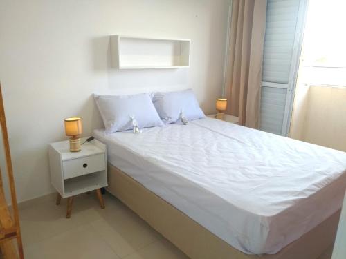 a bedroom with a white bed with two lamps on a night stand at APTo 300MTS DA PRAIA, VISTA PARA O MAR, CHURRASQUEIRA, WI-FI, AR CONDICIONADO, TOTALMENTE EQUIPADO in Ubatuba