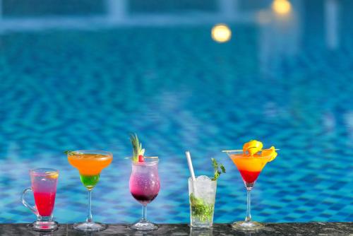 four cocktails sitting on a table next to a pool at Gold Beach Villa in Daman