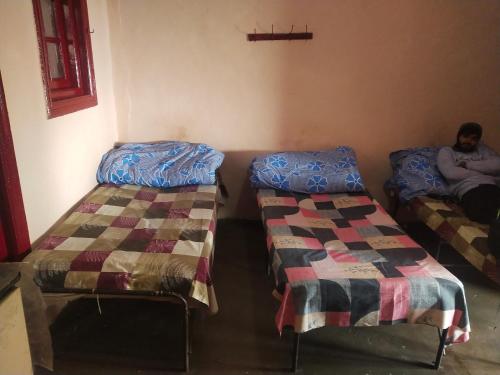 Deux lits dans une pièce avec un homme assis sur eux dans l'établissement Kumar Guest House, à Shimla