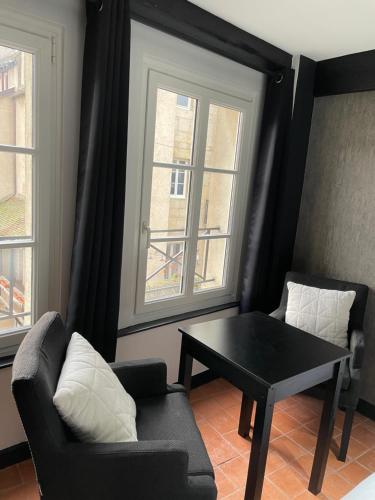 a living room with a table and a couch and two windows at Studio au Moulin " Design Noir " Vue Unique in Dole