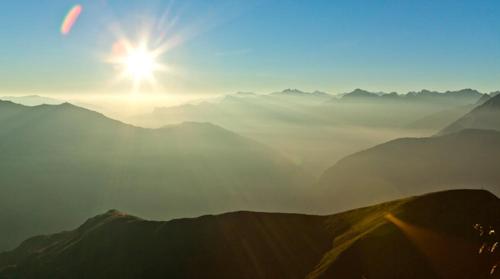 a sun is shining over a mountain range with clouds at Hotel Restaurant Sidan in Schwendau