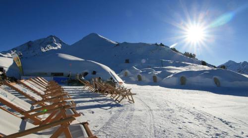 a row of wooden chairs in the snow with the sun at Hotel Restaurant Sidan in Schwendau