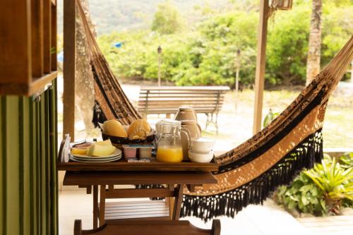 a hammock with a table with food and orange juice at Pousada Kainoa in Ilha do Mel