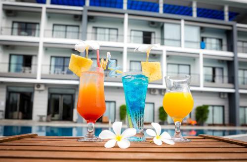 three drinks on a table with flowers and a pool at KEP BAY HOTEL & RESORT in Kep