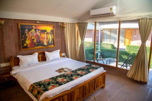 a bedroom with a large bed and a large window at Kurja Resort Balsamand in Jodhpur
