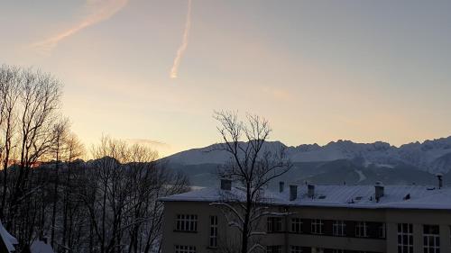 a building with a snowy roof with mountains in the background at Villa Fortuna - Regionalne apartamenty & SPA - Sauna, Grill, Jacuzzi z widokiem na Tatry in Zakopane