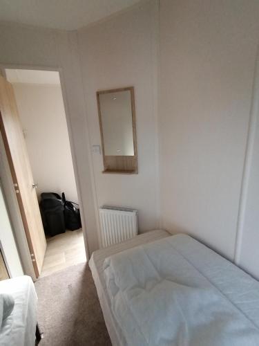 a white bedroom with a bed and a mirror at 69R Seawick 2 Bedroom Caravan . New for 2022 in Saint Osyth