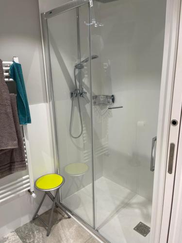 a glass shower with a yellow stool in a bathroom at Apartamentos La Estación in Ezcaray
