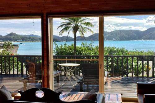a porch with a view of the ocean and a palm tree at Villa AdanRose Amami in Akagina