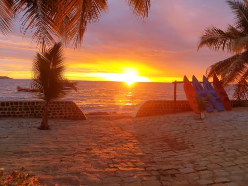 a sunset on the beach with surfboards and a palm tree at Anjiamarango Beach Resort in Nosy Be