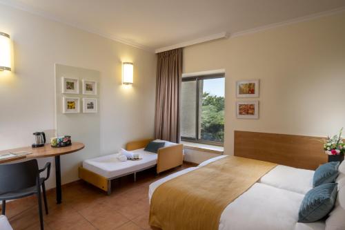 a hotel room with a bed and a desk and a window at Midreshet Hagolan Lodging in Haspin