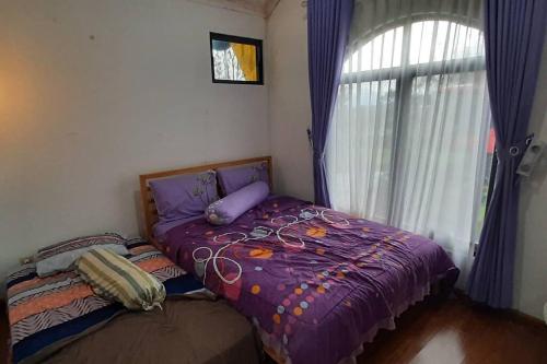 a bedroom with a bed with a purple comforter and a window at Villa Numismatik. Penginapan Unik yang Asri Alami in Cikundul