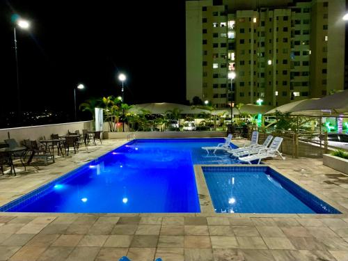 a blue swimming pool at night with chairs and tables at Lazer completo com Vistas de um Belo Horizonte in Belo Horizonte