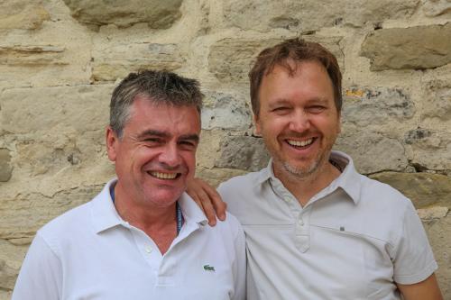 two men standing in front of a stone wall at La Maison du Passage - Chambres - Suites premium, Spa, Piscine et Restaurant in Martignargues