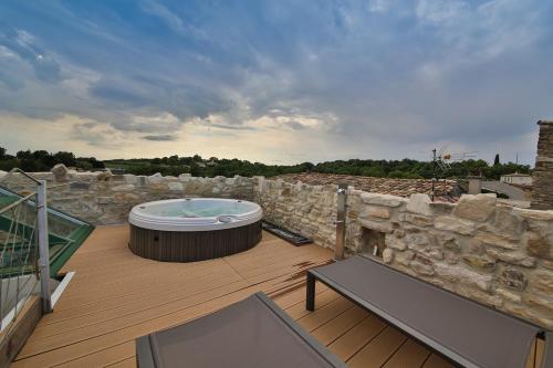 a deck with a hot tub and a stone wall at La Maison du Passage - Chambres - Suites premium, Spa, Piscine et Restaurant in Martignargues