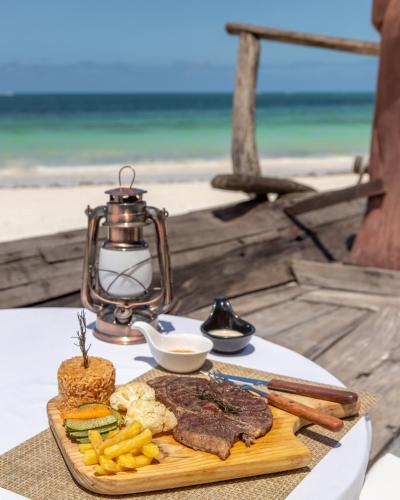 a plate of steak and french fries on a table near the beach at Kiwengwa Beach Resort in Kiwengwa