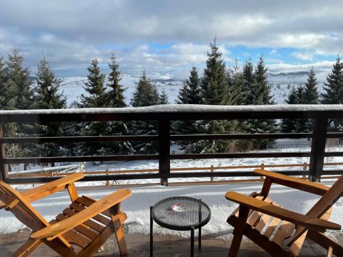 2 sedie e un tavolo sul balcone con neve di Family Nest Cabana in Statiunea Muntele Baisorii a Muntele Cacovei