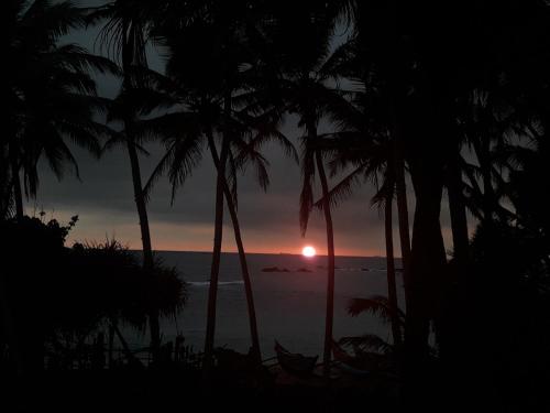 a sunset over the ocean with palm trees at SunRay Rest - Beach View Homestay in Mirissa
